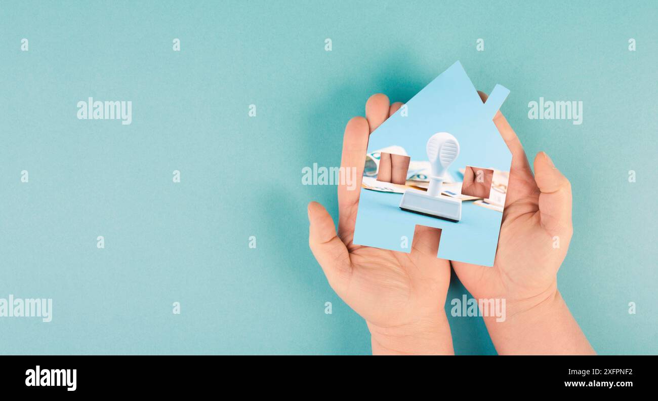 Ein Haus in der Hand halten mit Euro-Banknoten und einem Stempel, neues Grundsteuergesetz in Deutschland Stockfoto