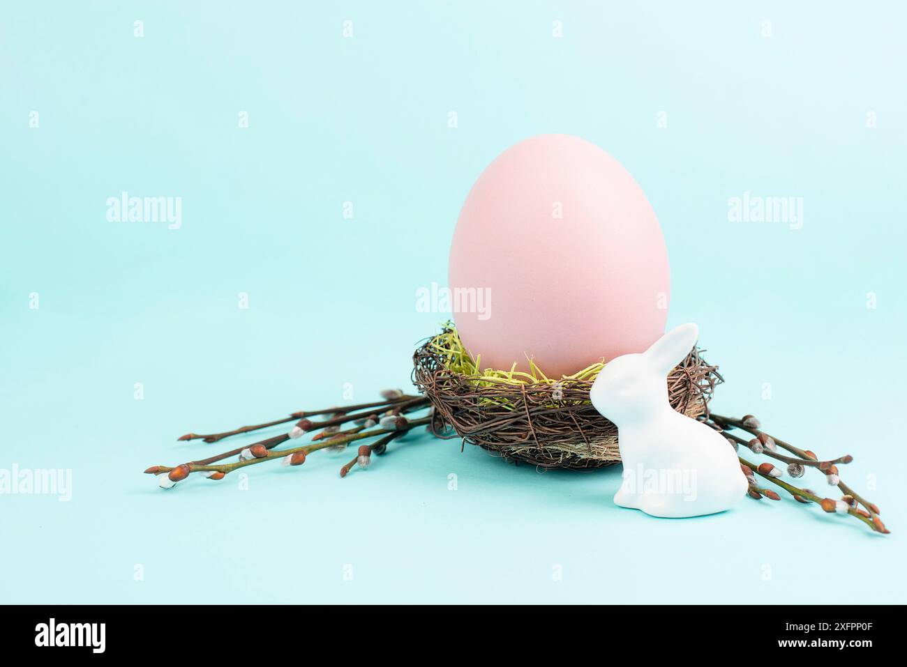 Osterhasen oder Kaninchen, die neben einem Weidennest mit bunten Eiern sitzen, Frühlingsferien Stockfoto
