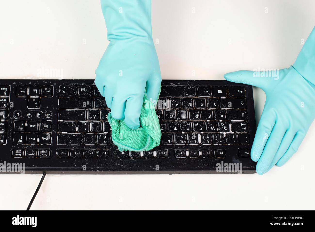 Reinigung der Computertastatur im Büro mit Gummischutzhandschuh, Peitschen mit Wasser und Seife, Reinigung staubiger und schmutziger Elektronik, Hausarbeit Stockfoto