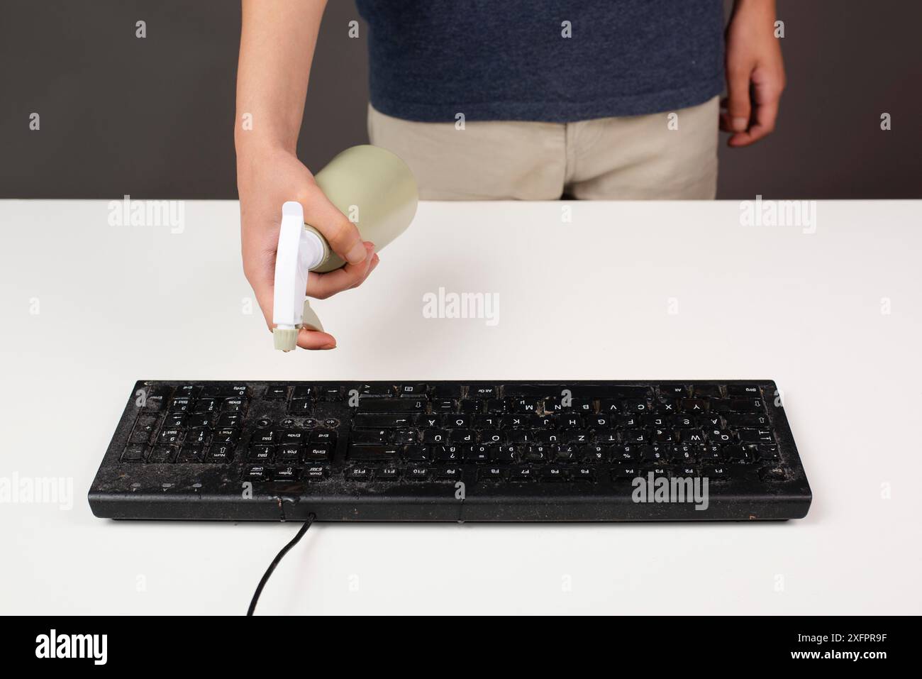 Reinigung der Computertastatur im Büro, Spritzen von Wasser mit einer Sprühflasche staubig und schmutzig Elektronik, Hausarbeit Stockfoto