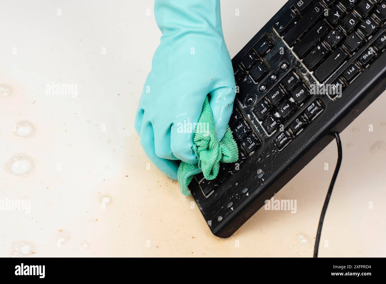 Reinigung der Computertastatur im Büro mit Gummischutzhandschuh, Peitschen mit Wasser und Seife, Reinigung staubiger und schmutziger Elektronik, Hausarbeit Stockfoto