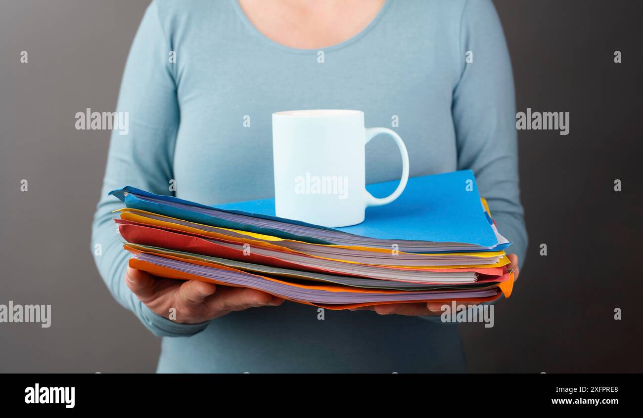 Frau mit einem Haufen Aktenmappen und einer Tasse Kaffee, Arbeit im Büro, Stress und Verbrennung, Schüler lernen für die Prüfung Stockfoto