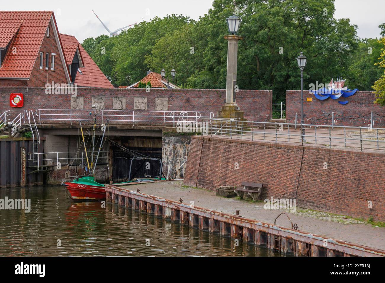 Ein kleines Hafengebiet mit einem rot-grünen Boot vor einer Backsteinmauer und grünen Bäumen im Hintergrund, wangerland, niedersachsen, deutschland Stockfoto