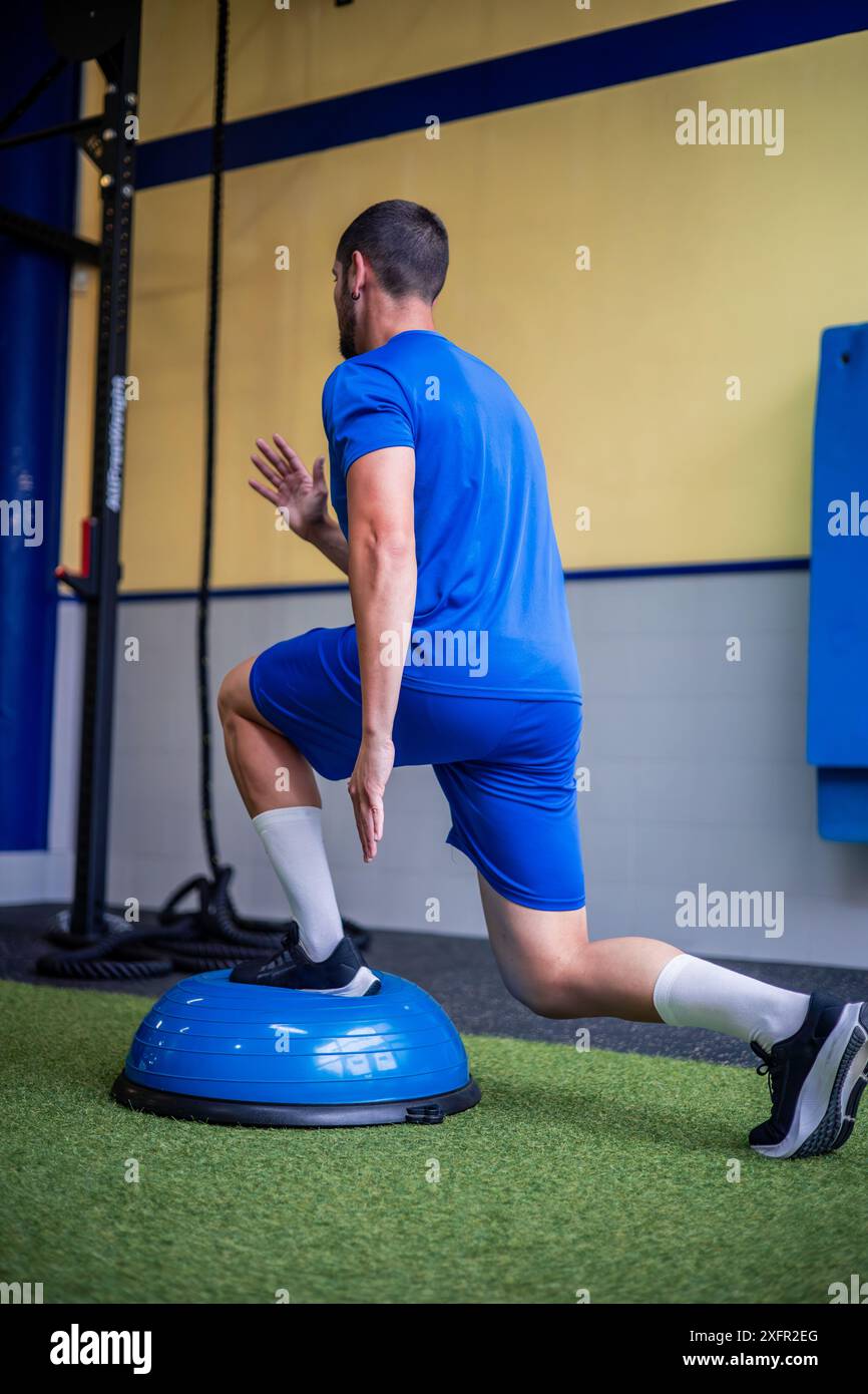 Junge Fitnessportler führen im Fitnessstudio Beinstärke- und Gleichgewichtsübungen mit einem Bosu-Ball durch. Dieses Bild unterstreicht den Fokus des Athleten auf Stabilität Stockfoto