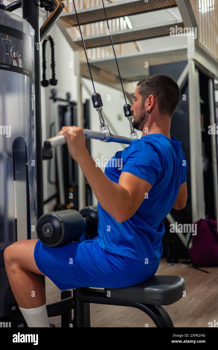 Ein junger Fitness-Enthusiast führt mit einem Pulldown-Training mit hohem Pulldown durch, um seine Rückenmuskeln im Fitnessstudio zu trainieren. Diese Übung Dämon Stockfoto
