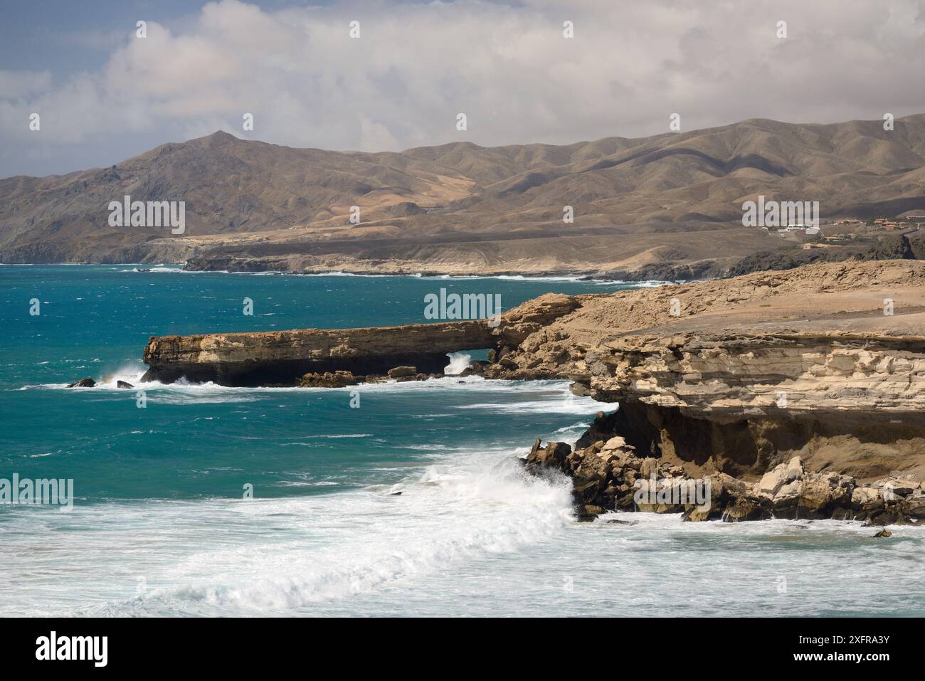 Klippen mit Schichten aus vulkanischer Asche, Bimsstein und Lava aus aufeinanderfolgenden Eruptionen, die stark vom Meer untergraben und erodiert wurden, La Pared, Fuerteventura, Kanarische Inseln, Mai. Stockfoto