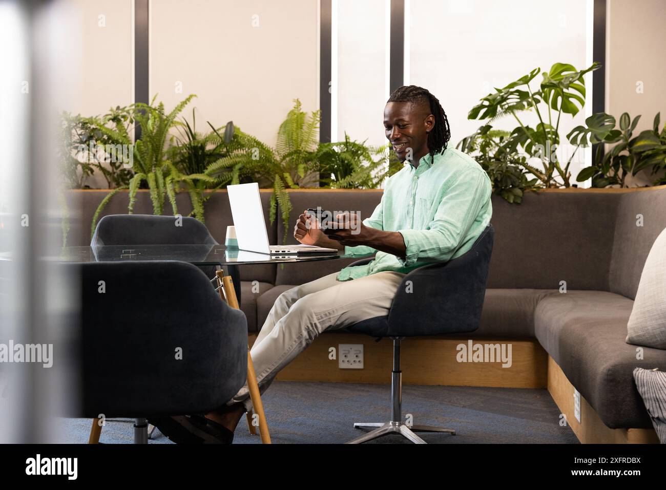 Mit Smartphone und Laptop, Mann, der in einem modernen Büro mit Pflanzen arbeitet Stockfoto