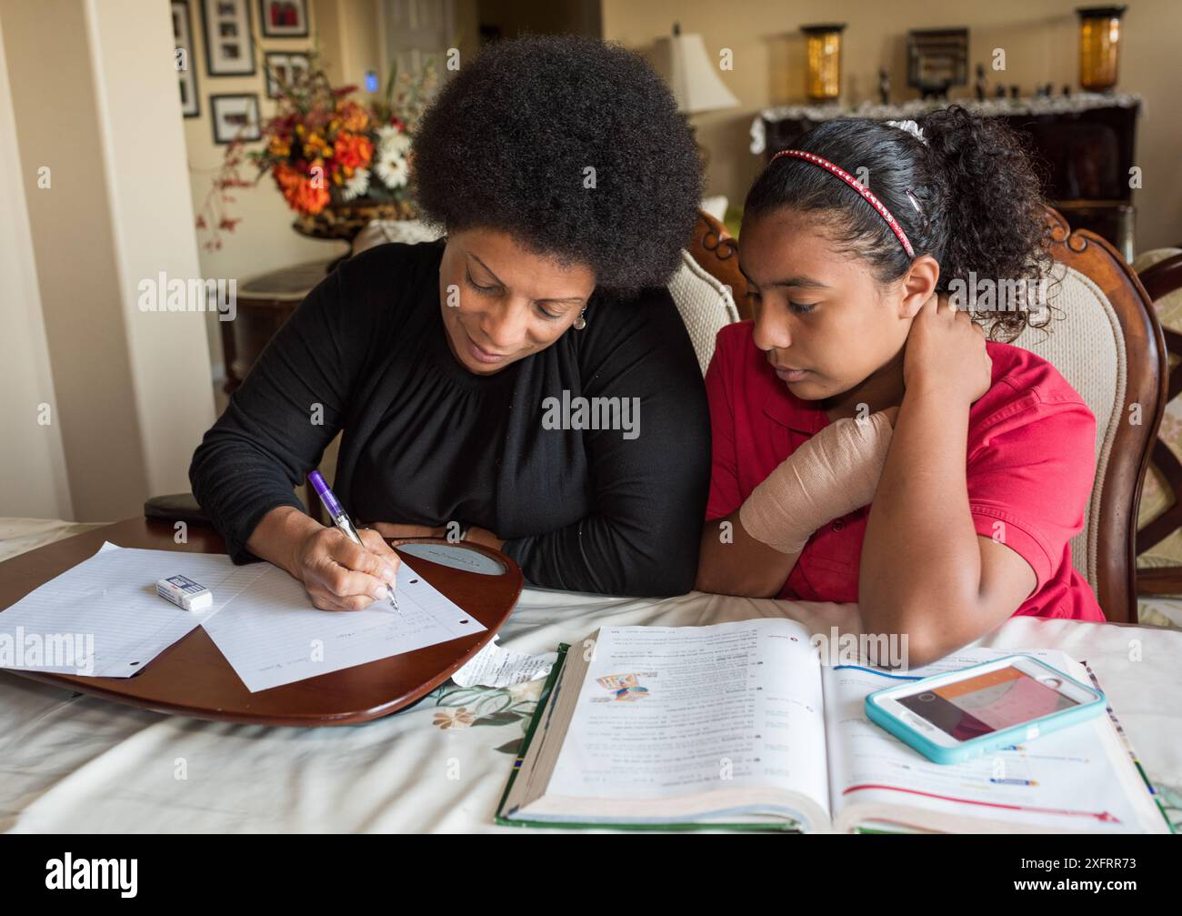 Afroamerikanische Mutter hilft Tochter bei Hausaufgaben am Esstisch. Stockfoto