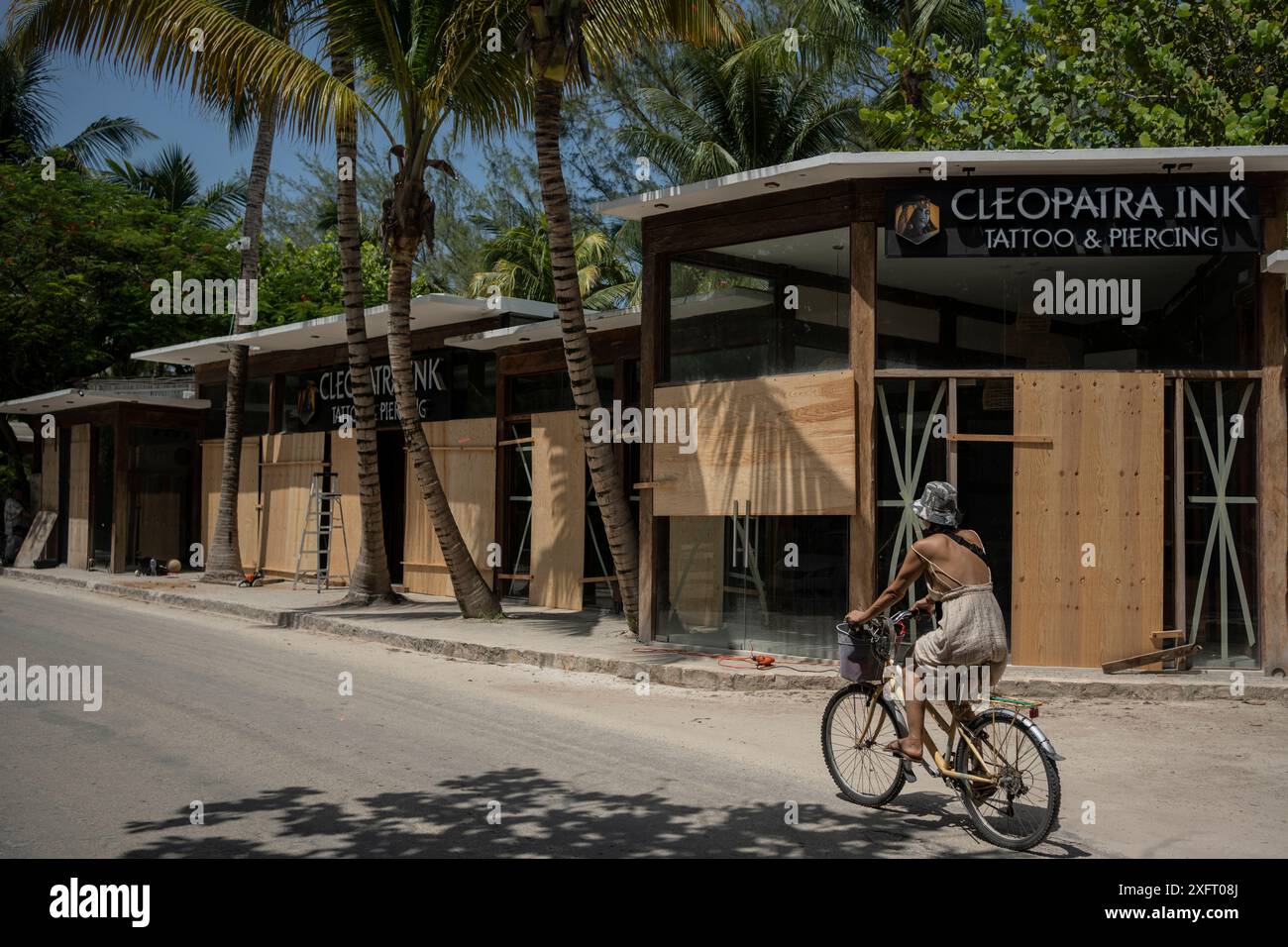 Tulum, Mexiko. Juli 2024. Eine Frau fährt mit dem Fahrrad vor einem Laden, der von Holzbrettern vor den Auswirkungen des Hurrikans Beryl geschützt ist. Der atlantische Hurrikan wird voraussichtlich am Freitagabend Hurrikan 1 an der Ostküste der Halbinsel Yucatán erreichen. Experten erwarten starke Winde und Regenfälle sowie gefährliche Sturmfluten. Quelle: Felix Marquez/dpa/Alamy Live News Stockfoto