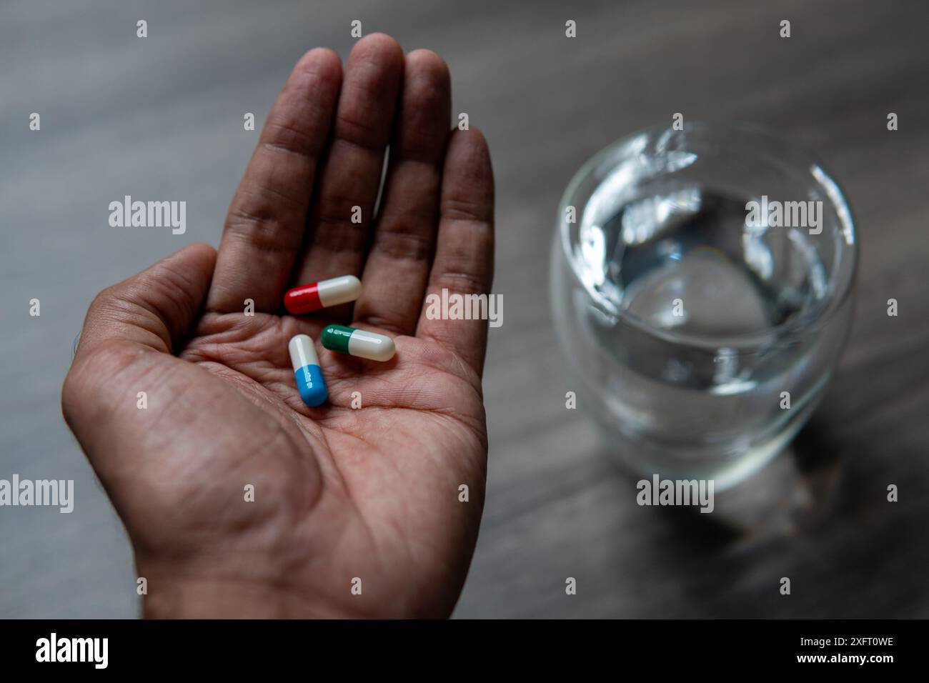 Ein Nahaufnahme-Foto einer Person, die eine bunte Pille und ein Glas Wasser in der Hand hält. Medizin- und Gesundheitskonzept. Stockfoto