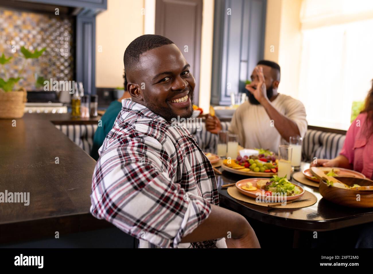 Ein lächelnder Mann, der mit verschiedenen Freunden am Esstisch Essen genießt, Lachen und Essen teilt Stockfoto