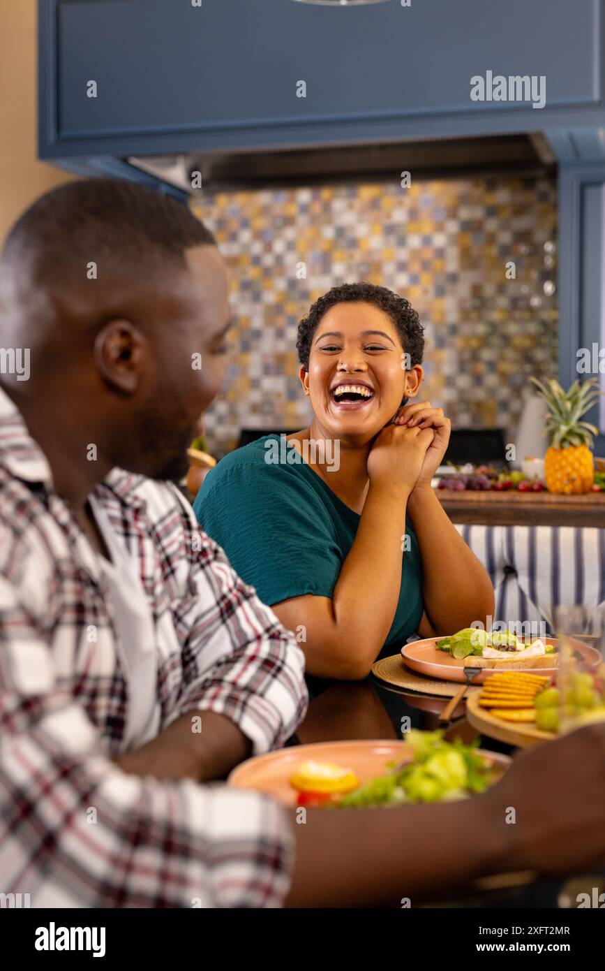 Verschiedene Freunde, die gemeinsam essen, lachen und sich am Esstisch unterhalten Stockfoto