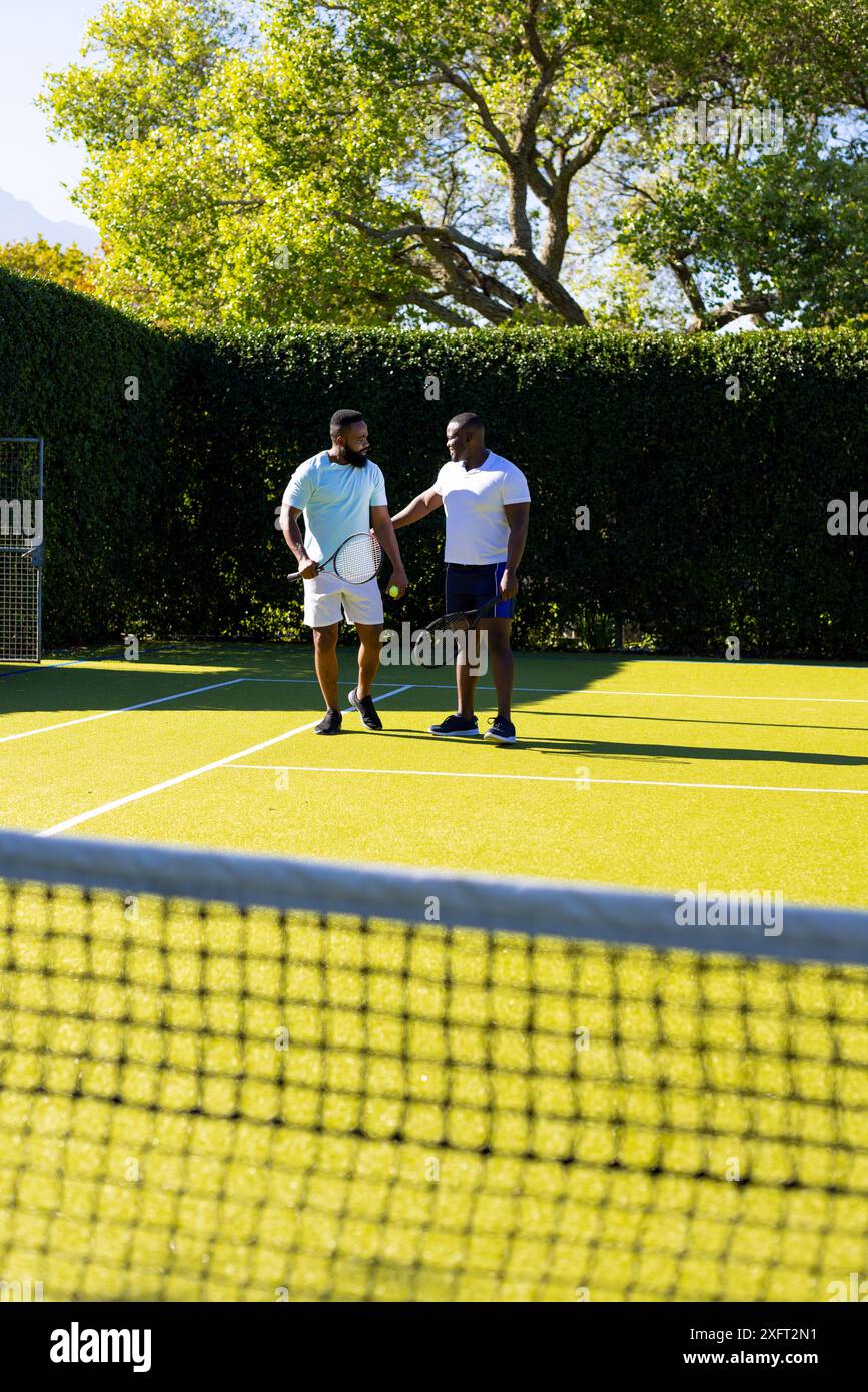 Tennis spielen auf dem Platz, zwei verschiedene Freunde halten Schläger und unterhalten sich miteinander Stockfoto