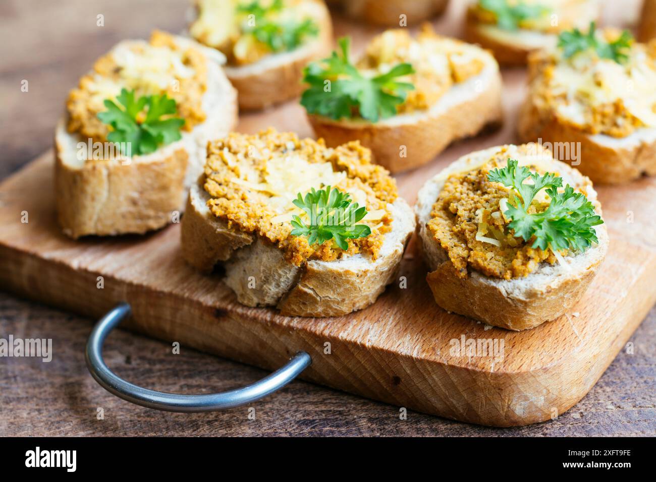 Baguette-Scheiben mit Karotten-Walnussaufstrich und veganem Käse auf einem Schneidebrett. Stockfoto