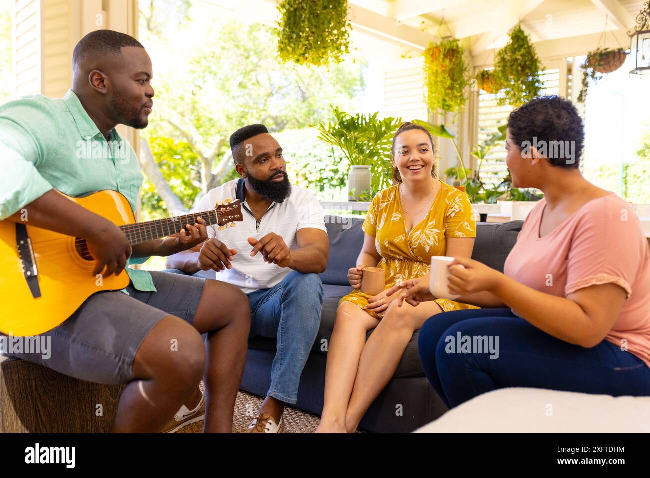 Gitarre spielen und Kaffee genießen, verschiedene Freunde, die sich auf der Terrasse entspannen Stockfoto