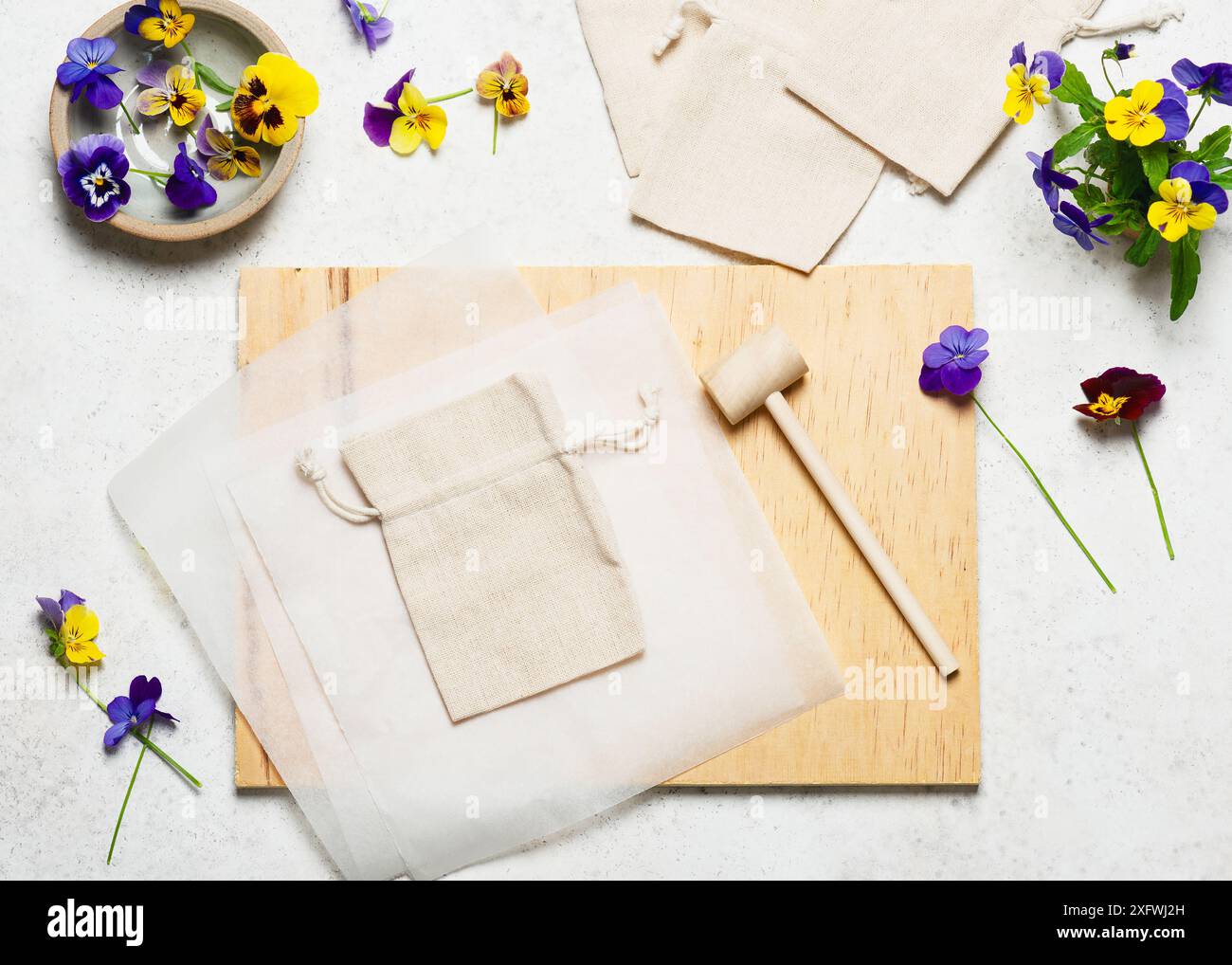 Blick von oben auf den Arbeitsplatz mit Stofftaschen, Stiefmütterchen, Holzhammer, transparenten Papieren, Holzblock. Schritt für Schritt einen Baumwollbeutel erstellen Stockfoto