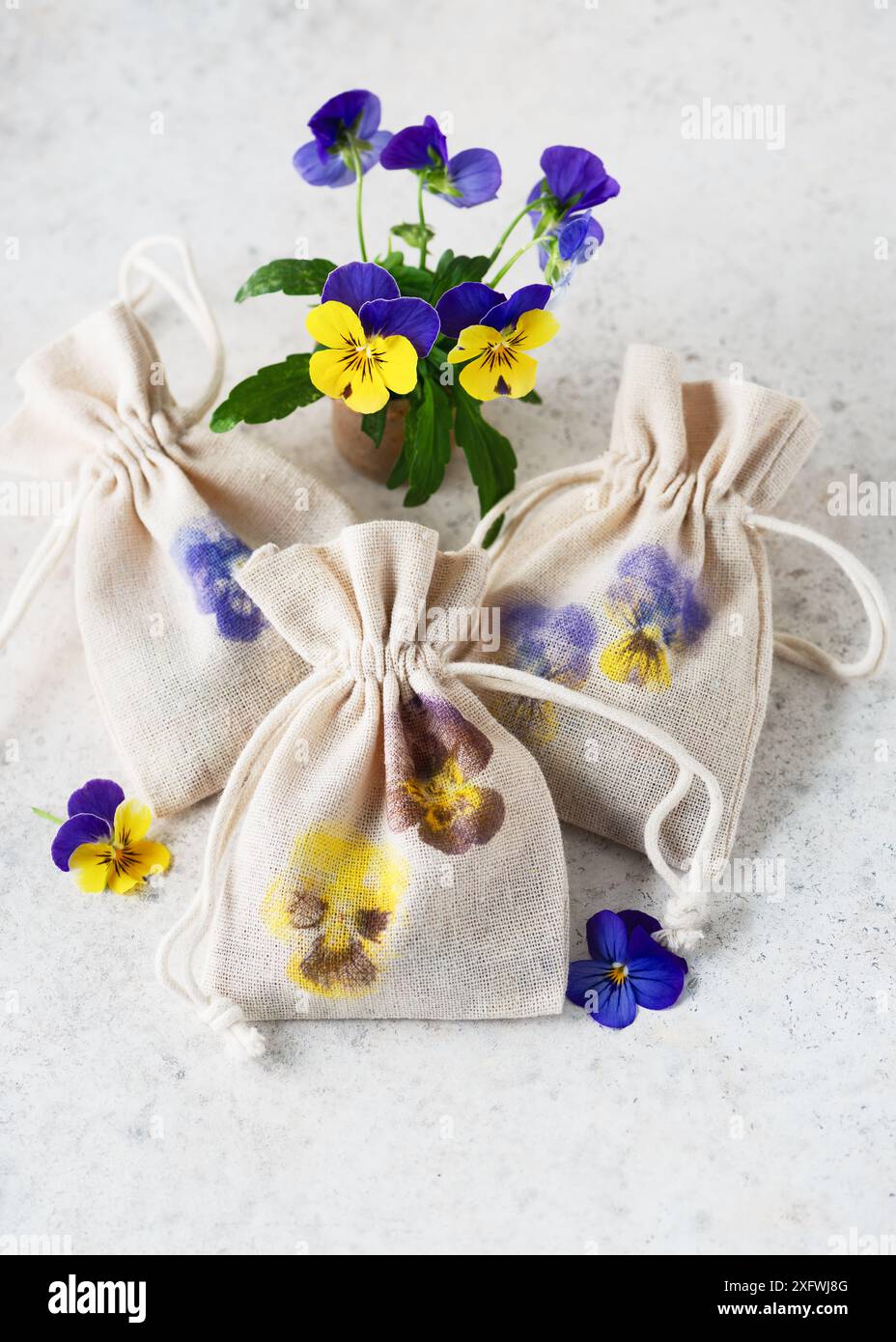 Schöne handgefertigte Stofftaschen mit gehämmerten Stiefmütterchenmotiven als kleines Geschenk für den Muttertag oder Ostern. Naturmaterial-Bastelkonzept für Kinder. Stockfoto