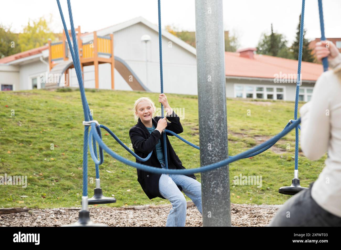 Glücklicher Teenager, der Spaß auf der Schaukel auf dem Schulhof mit einem Freund hat Stockfoto