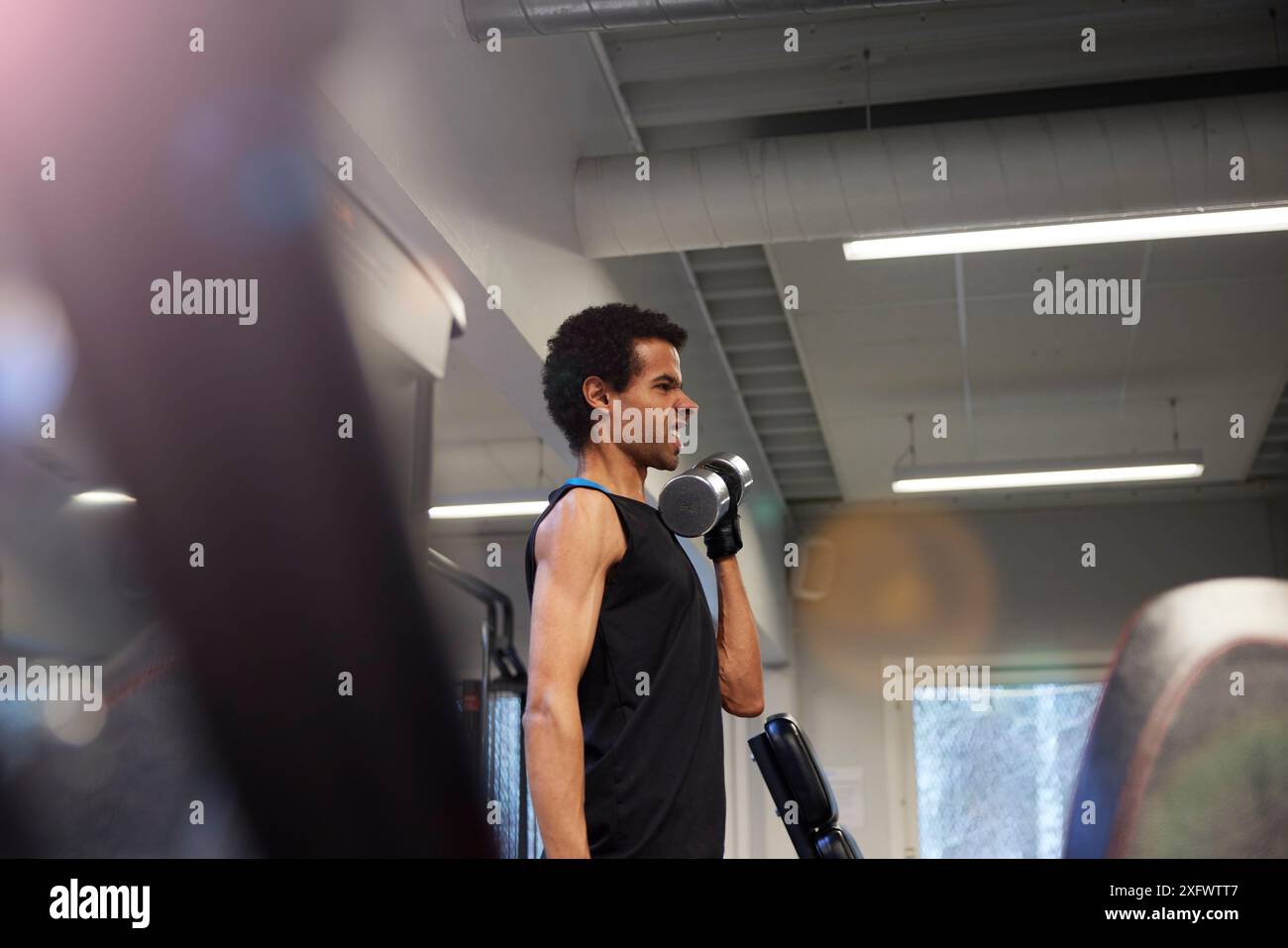 Junger Mann, der mit Hantel trainiert, während er im Fitnessstudio ein Gesicht macht Stockfoto