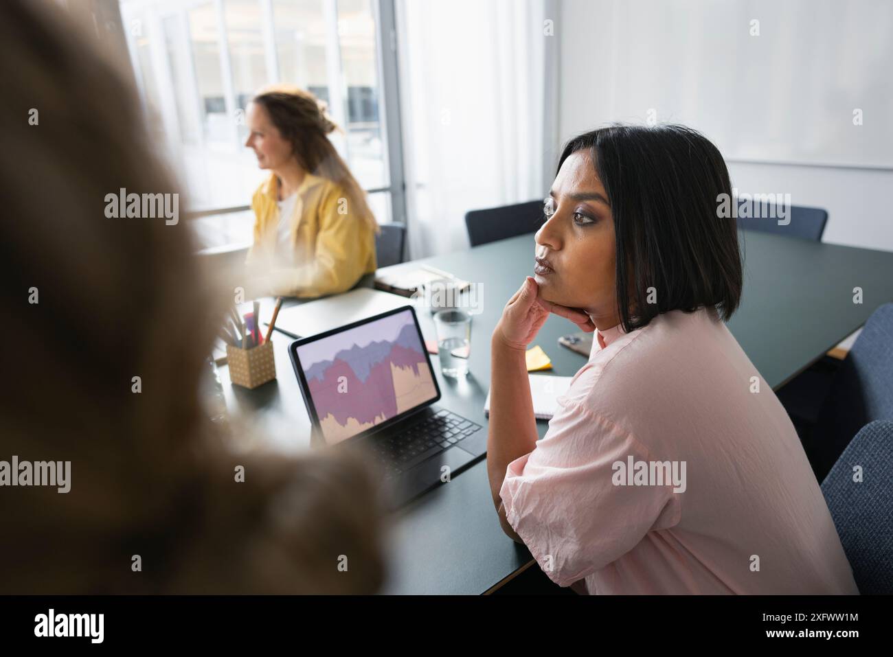 Ernsthafte Geschäftsfrau, die wegschaut, während sie im Büro über dem Tisch sitzt Stockfoto