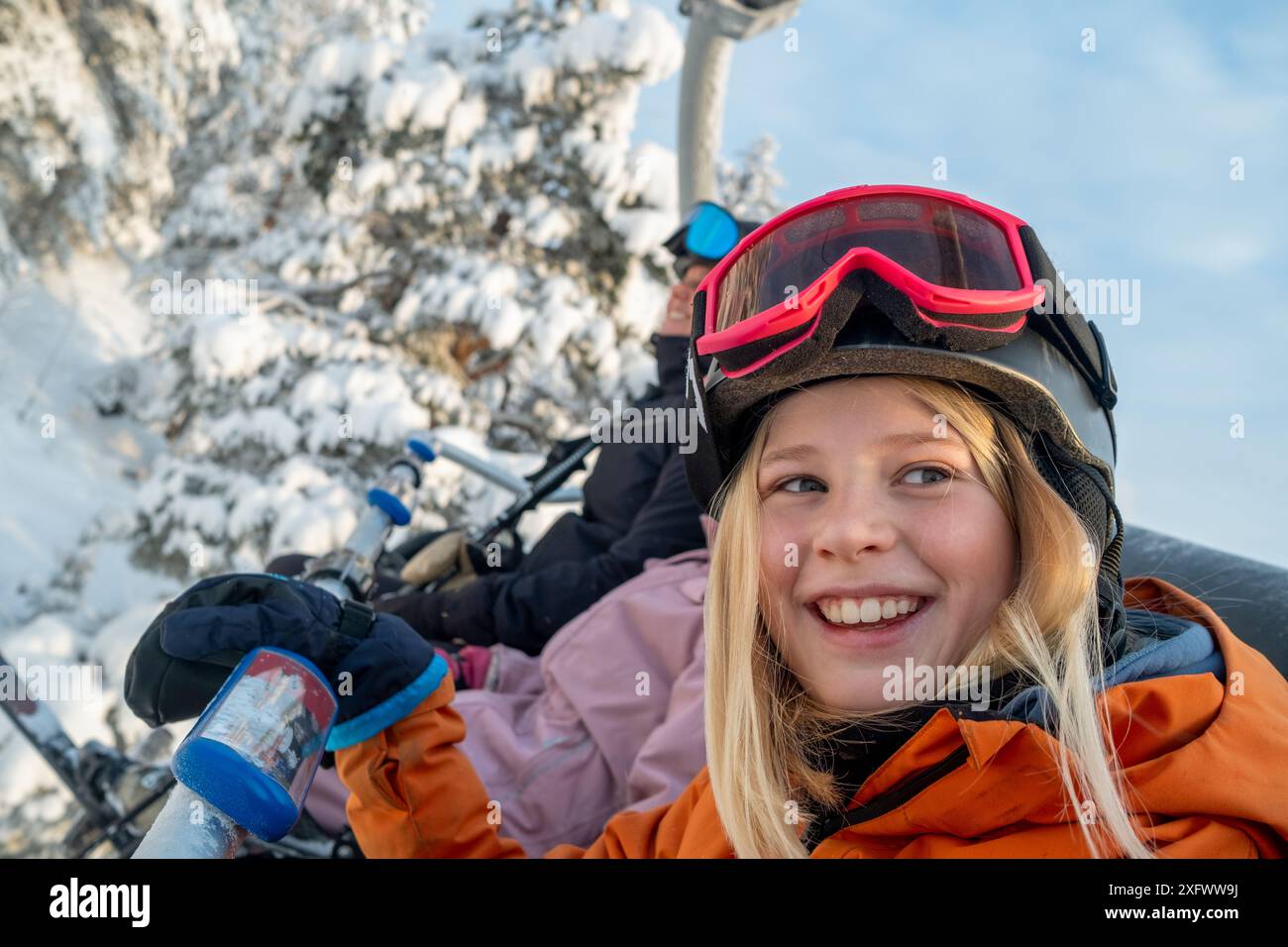 Lächelndes Mädchen mit Helm und Schutzbrille, das auf dem Skilift sitzt Stockfoto