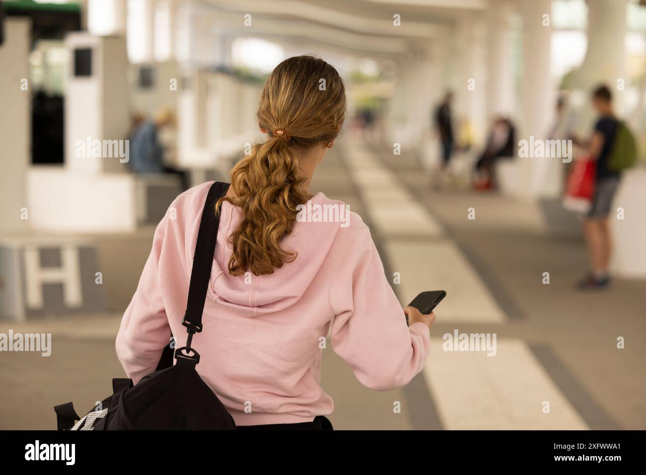 Rückansicht einer Athletin, die ihr Handy hält, während sie ihre Tasche im Park trägt Stockfoto