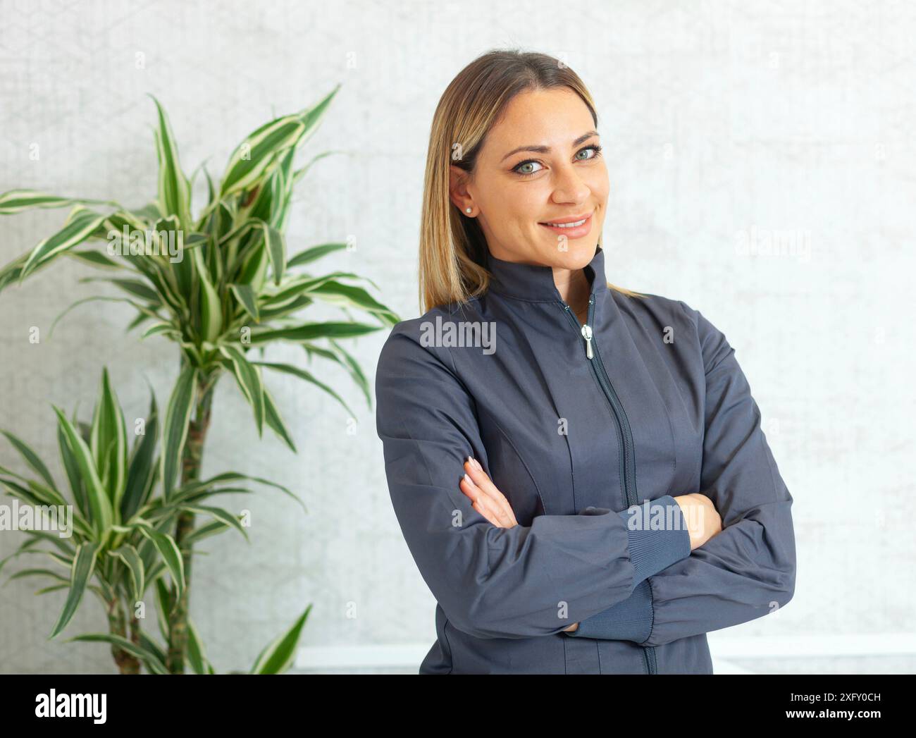 Porträt einer schönen lächelnden Frau mit blonden Haaren und grünen Augen. Sie trägt professionelle medizinische Kleidung, die für den Einsatz in medizinischen, dextristischen und ästhetischen Bereichen vorstellbar ist. Stockfoto