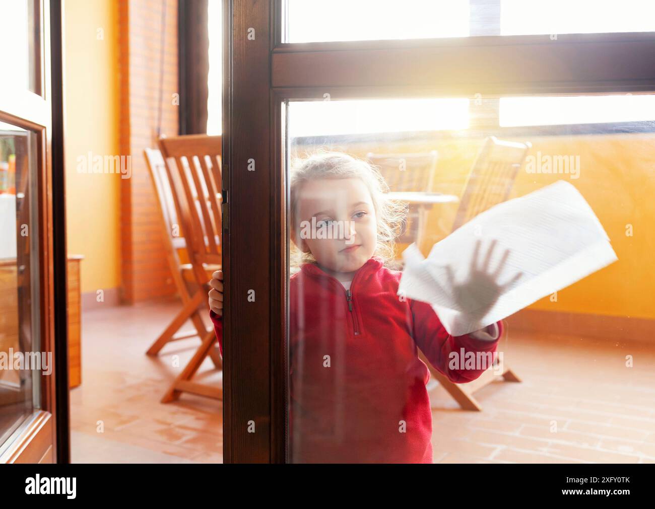 Das dreijährige Mädchen hilft bei der Haushaltsreinigung. Sie reinigt die Fenster mit einem Blatt Papier. Idee, die Zeit während der Kovid-19-Coronavirus-Quarantänezeit zu verstreichen. Stockfoto