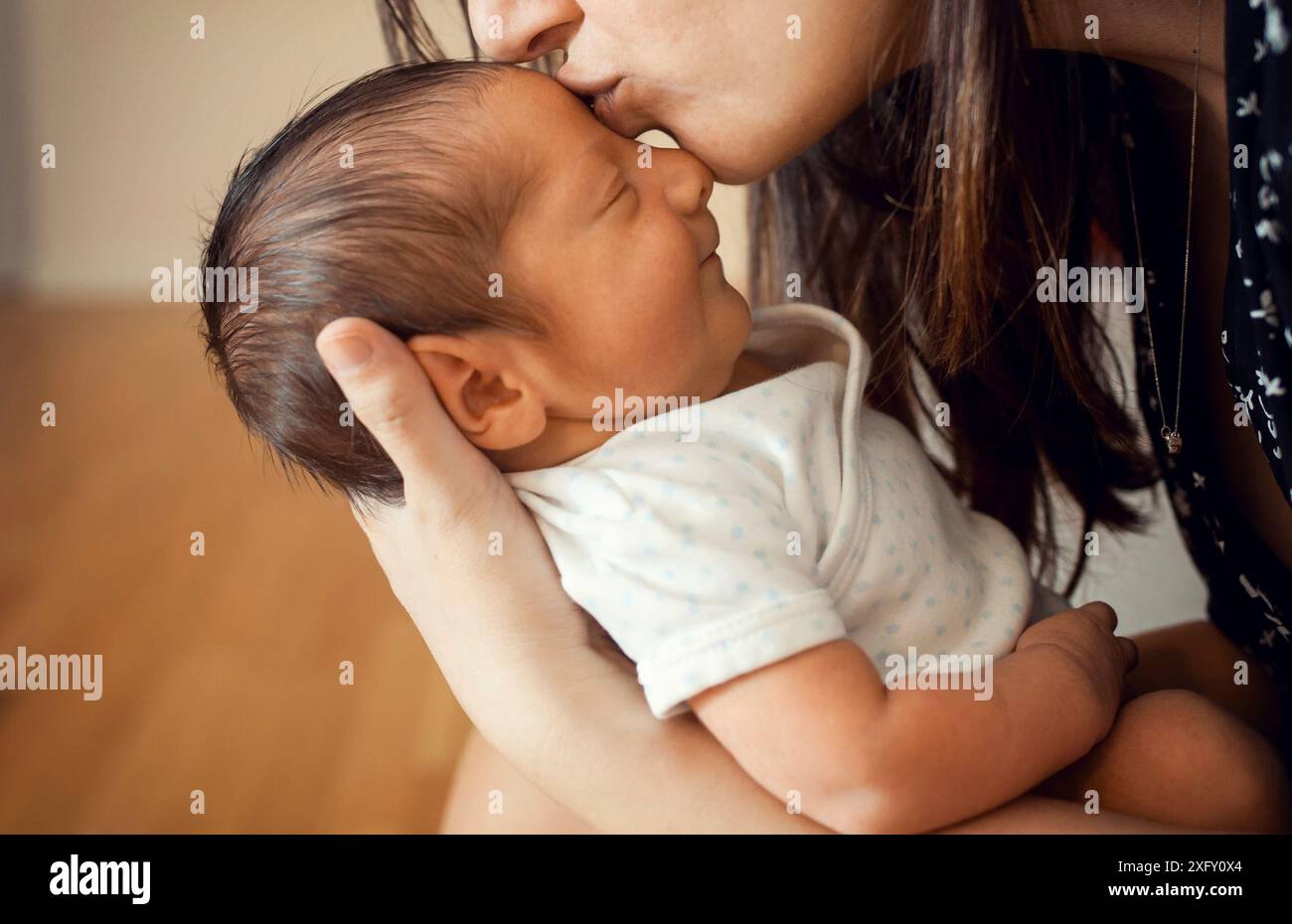 Ein paar Tage altes Baby wird von seiner Mutter auf die Stirn geküsst. Es lächelt, wenn er den Boden auf sich selbst spürt. Stockfoto