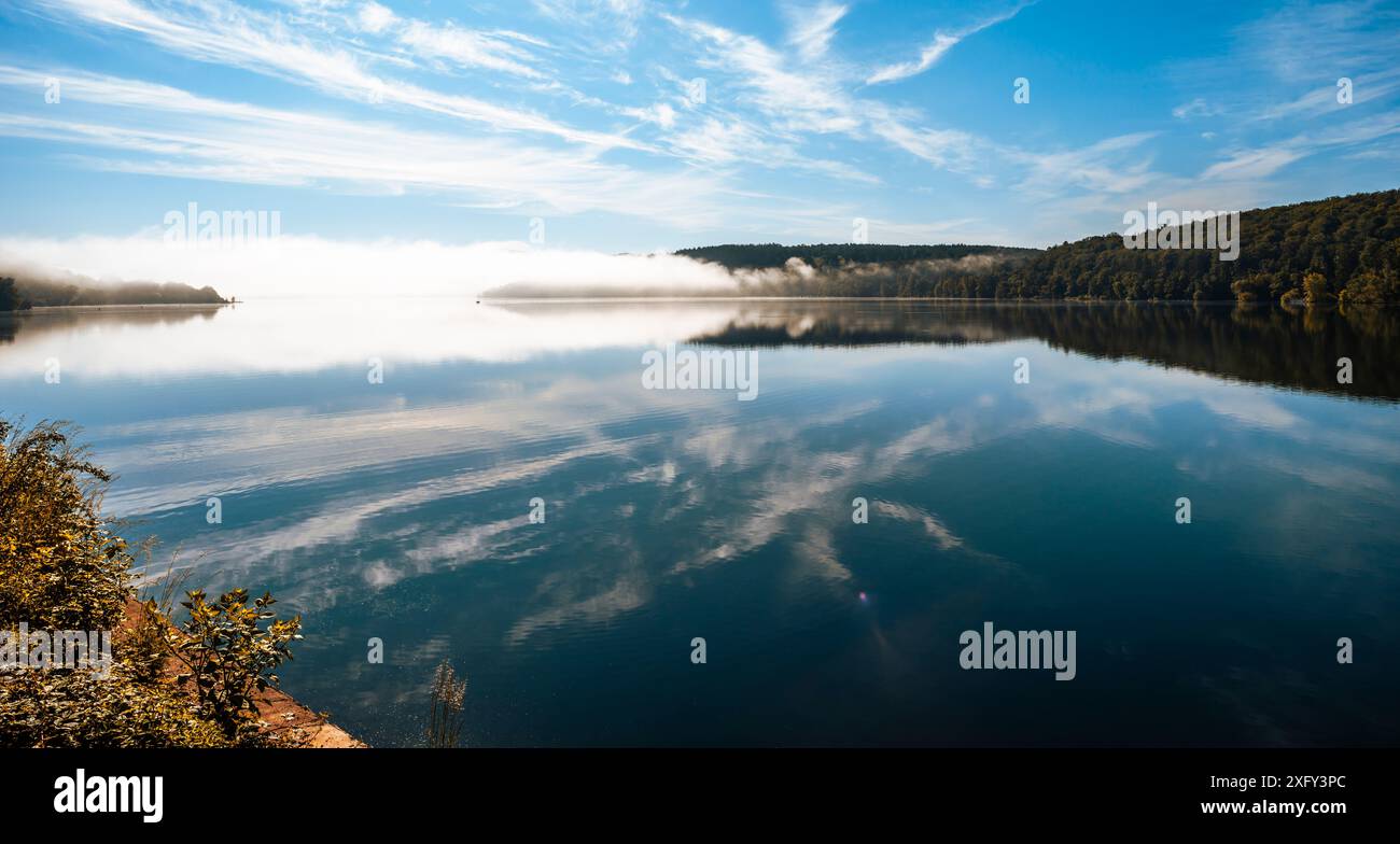 Edersee an einem sonnigen Morgen, leichter Nebel in der Ferne, Reflexion auf dem ruhigen Wasser. Bezirk Waldeck-Frankenberg, Hessen, Deutschland. Stockfoto