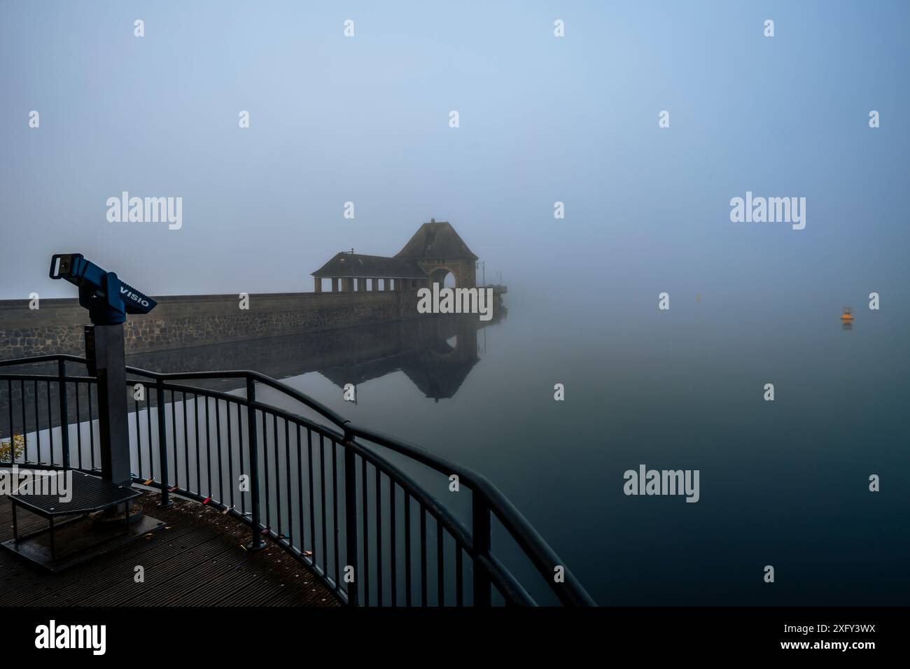 Dammmauer am Edersee im Morgennebel, Reflexion im ruhigen Wasser, eine gelbe Boje am Bildrand. Fernglas im Vordergrund anzeigen. Bezirk Waldeck-Frankenberg, Hessen, Deutschland. Stockfoto