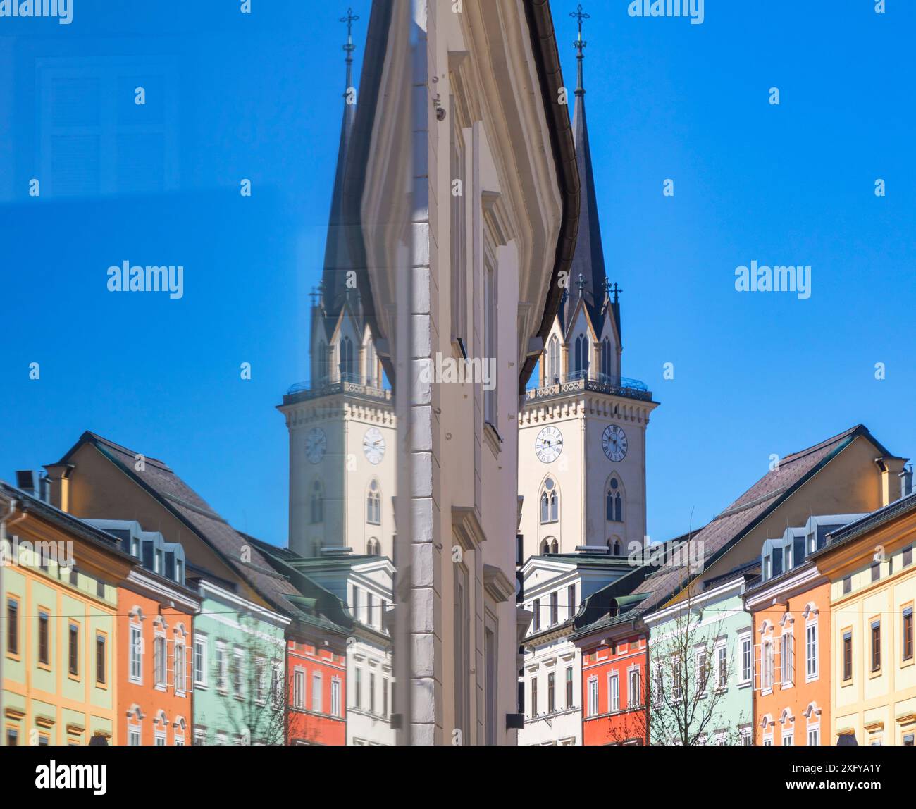 Symmetrie von bunten Gebäuden und Kirchturm der Pfarrkirche spiegelt sich in einem Schaufenster der Altstadt von villach, kärnten, österreich Stockfoto