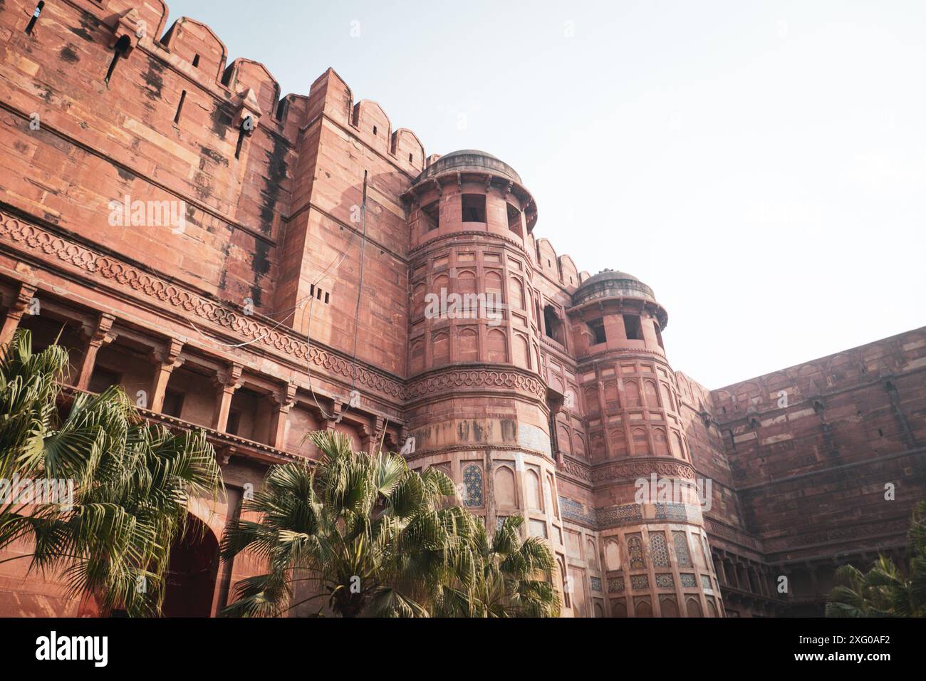 Ein Blick auf das historische Agra Fort mit seiner roten Sandsteinarchitektur und üppigen grünen Palmen Stockfoto