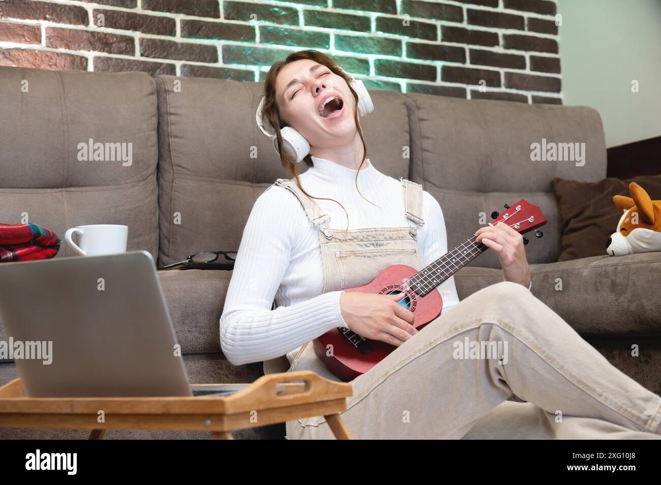 Musikunterricht aus der Ferne, Ukulele spielen oder Gesang unterrichten, singen. Hipster-Schüler zeichnen Lektion auf oder lernen mit Laptop-Webcam im Sitzen Stockfoto