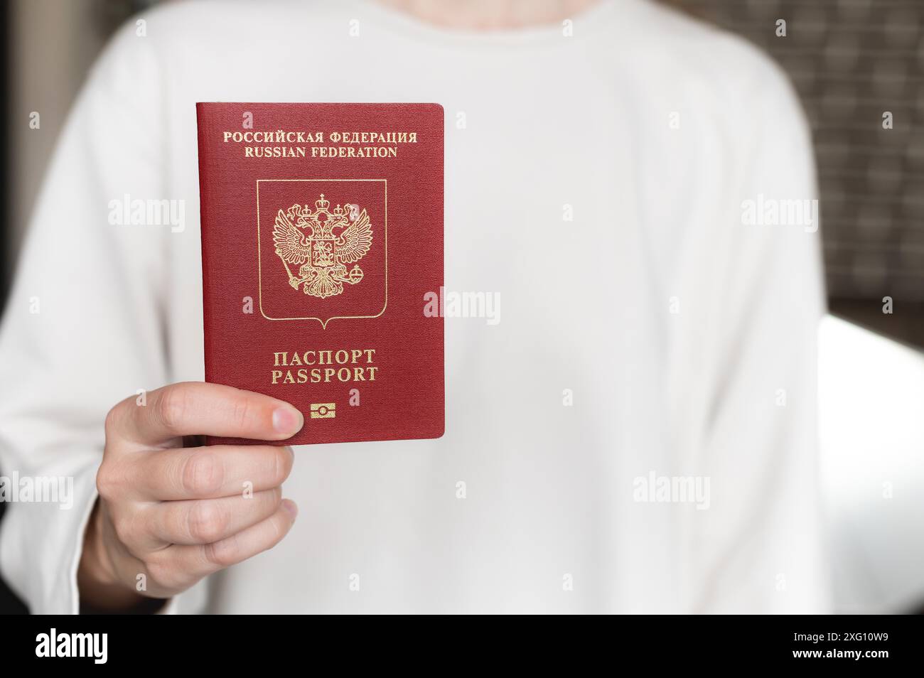Ausländischer Pass der Russischen Föderation. Menschliche weibliche Hand mit russischem Pass Nahaufnahme auf dem Hintergrund eines weißen Pullovers, selektiver Fokus Stockfoto