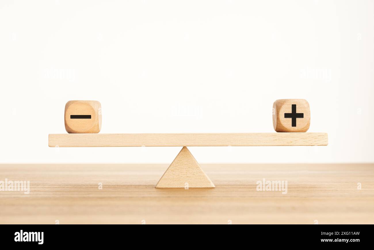 Plus- und Minus-Balance-Konzept. Positive und negative Symbole auf Holzblöcken sind auf einer hölzernen Wippe im Gleichgewicht. Speicherplatz kopieren Stockfoto