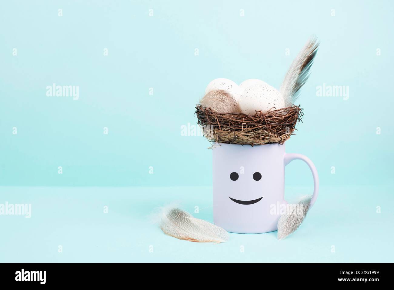 Becher mit osterei, Vogelfedern und einem lächelnden fröhlichen Gesicht, Frühjahrsgrußkarte Stockfoto