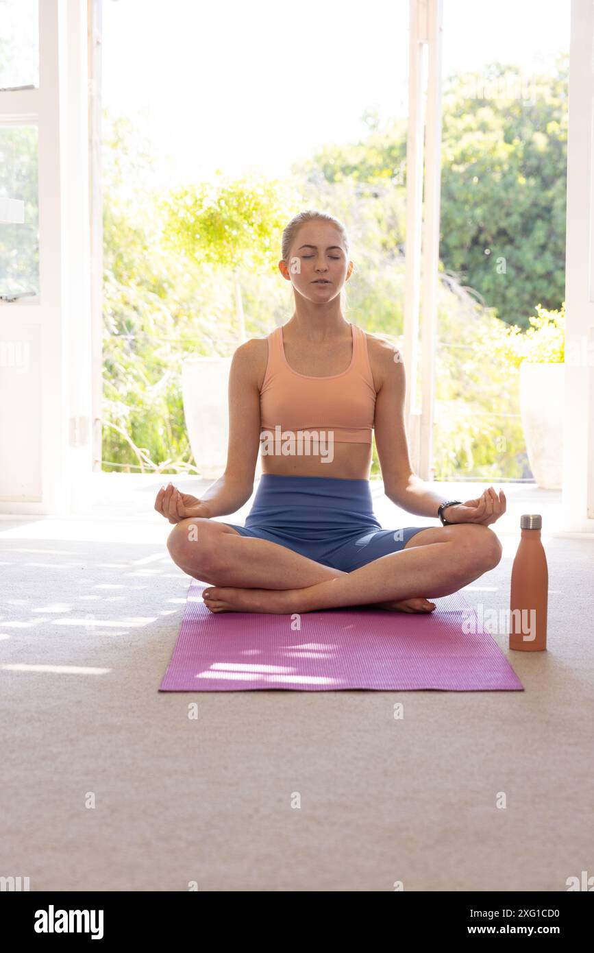 Meditation auf Yogamatte, Frau sitzt im Kreuz mit einer Wasserflasche in der Nähe Stockfoto