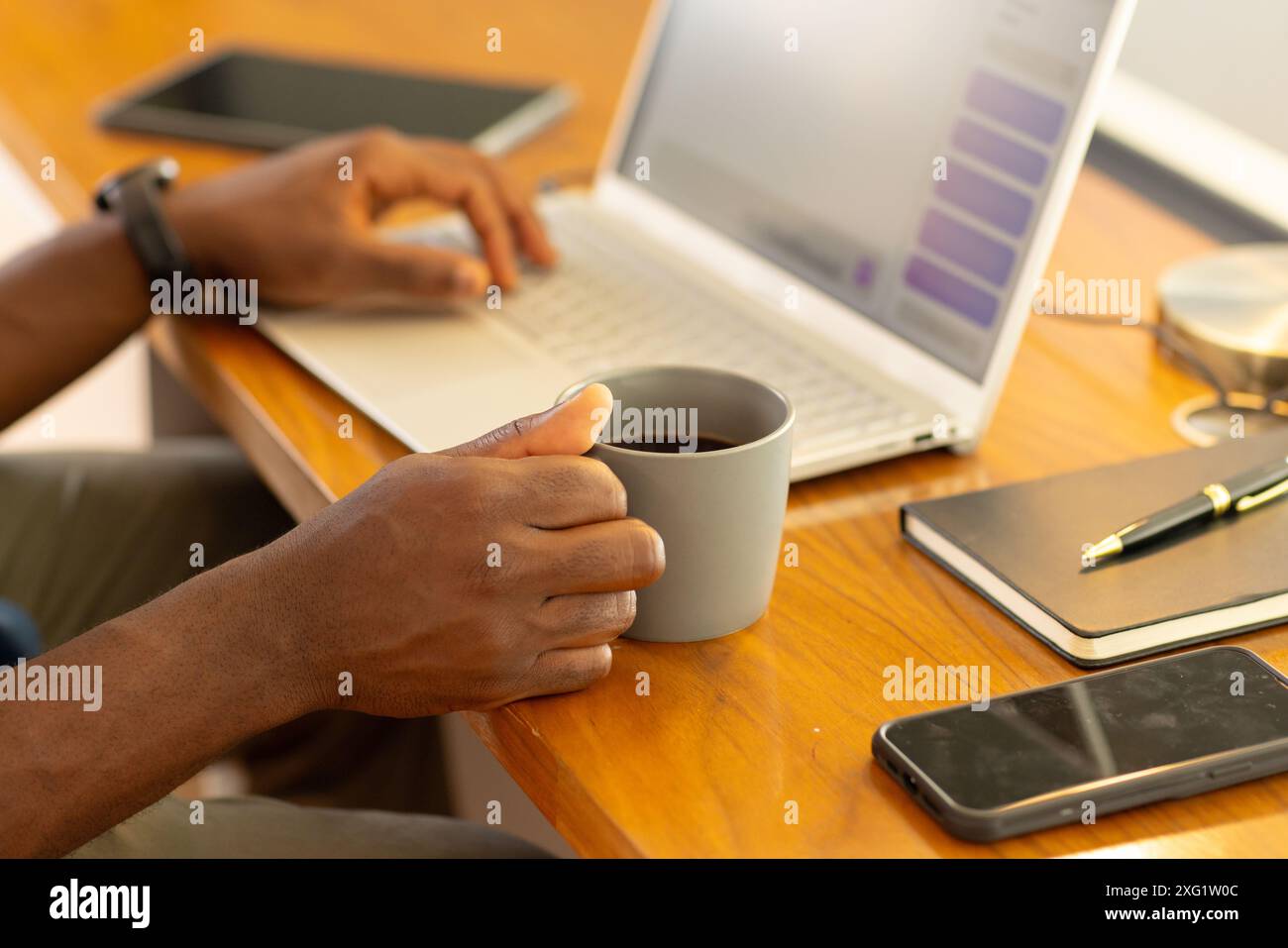 Eine Kaffeetasse halten, Mann, der am Laptop am Schreibtisch im Heimbüro arbeitet Stockfoto