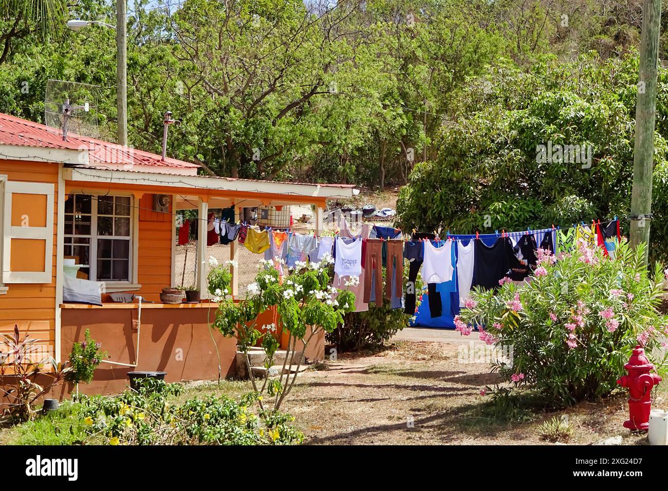 Die Wäsche hängt an der Wäscheleine vor einem bunten Holzhaus im karibischen Dorf in Antigua Stockfoto