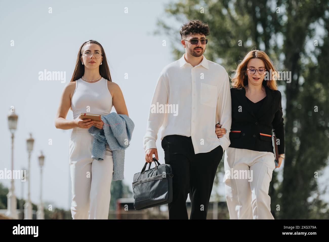 Geschäftskollegen, die im Freien unterwegs sind und verschiedene Gegenstände in einem professionellen Umfeld halten Stockfoto