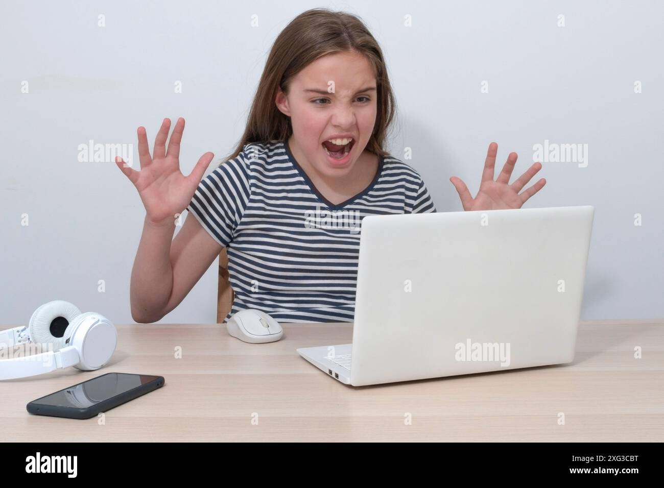 Ein Teenager-Mädchen mit einem Computer ist wütend auf einen Gesprächspartner im Internet. Nicht funktionierender Laptop. Gestreiftes T-Shirt, negative Stimmung Stockfoto