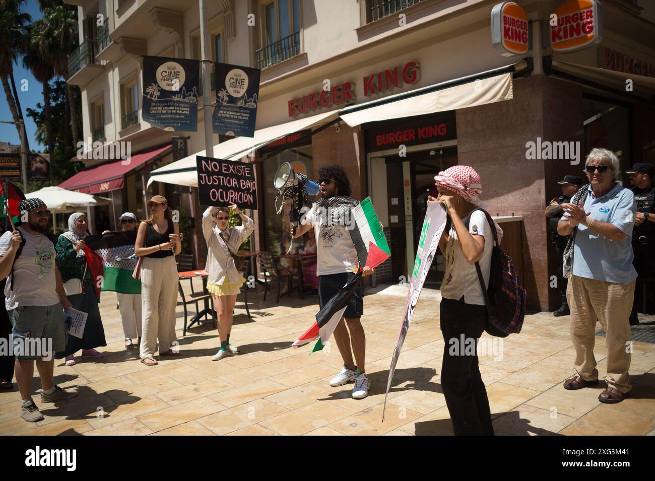 Malaga, Spanien. Juli 2024. Ein Mann, der mit einer palästinensischen Flagge gewickelt ist, wird auf einem Megaphon vor dem Restaurant Burger King sprechen sehen, während er an einer solidarischen Demonstration mit dem palästinensischen Volk teilnimmt. Unter dem Motto "gegen den Völkermord und die zionistische Besatzung" fordern Dutzende von Menschen angesichts der anhaltenden Konflikte zwischen Israel und der Hamas ein Ende des Waffenhandels und der Handelsbeziehungen mit Israel. Quelle: SOPA Images Limited/Alamy Live News Stockfoto
