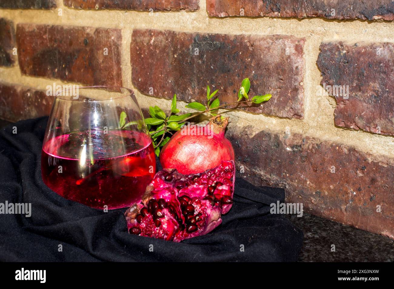 Rustikales Stilleben von Granatapfel Gin and Tonic, umgeben von Granatapfelfrüchten und Laub. Stockfoto