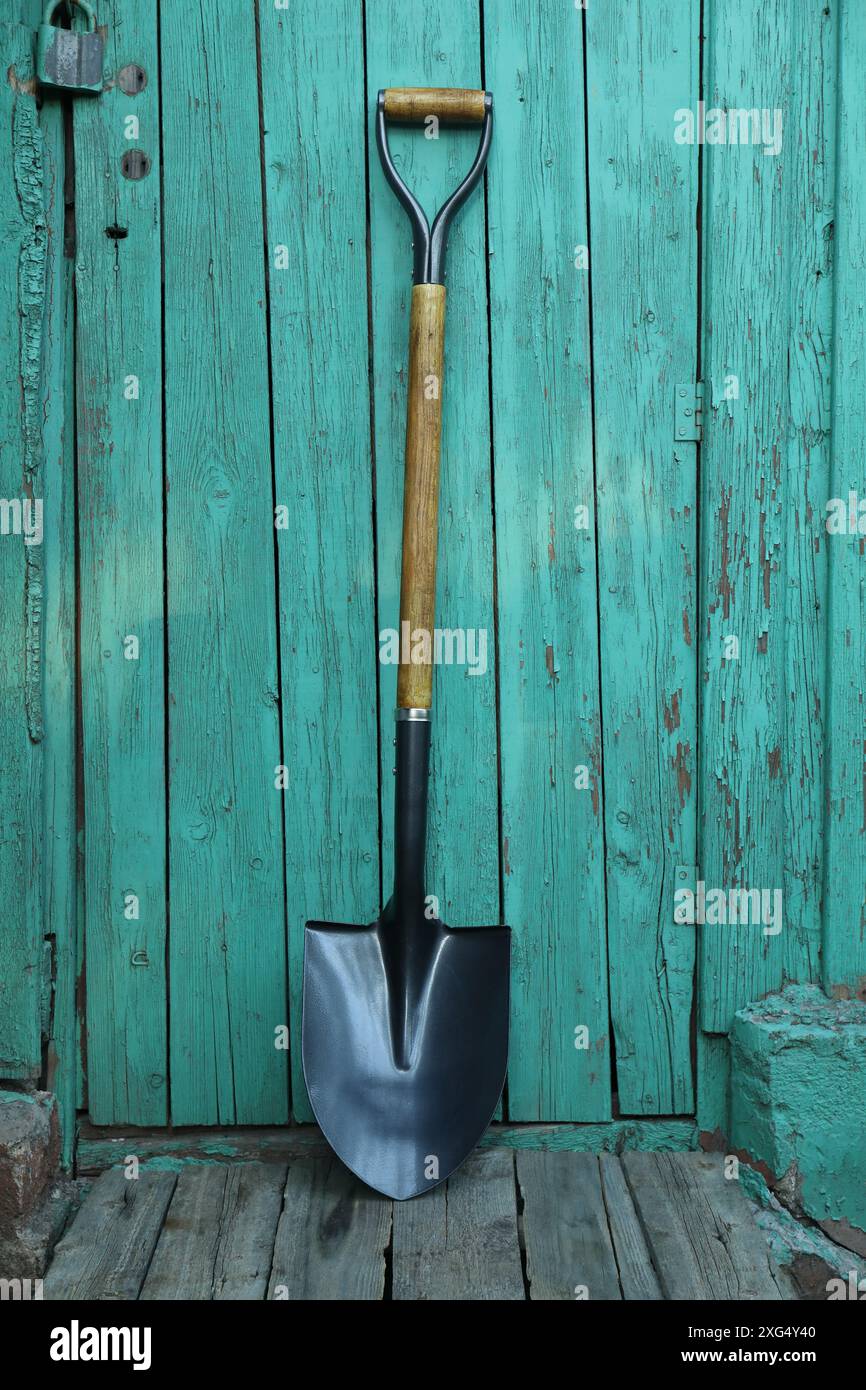 Metallschaufel in der Nähe einer türkisfarbenen Holzwand. Gartenwerkzeug Stockfoto