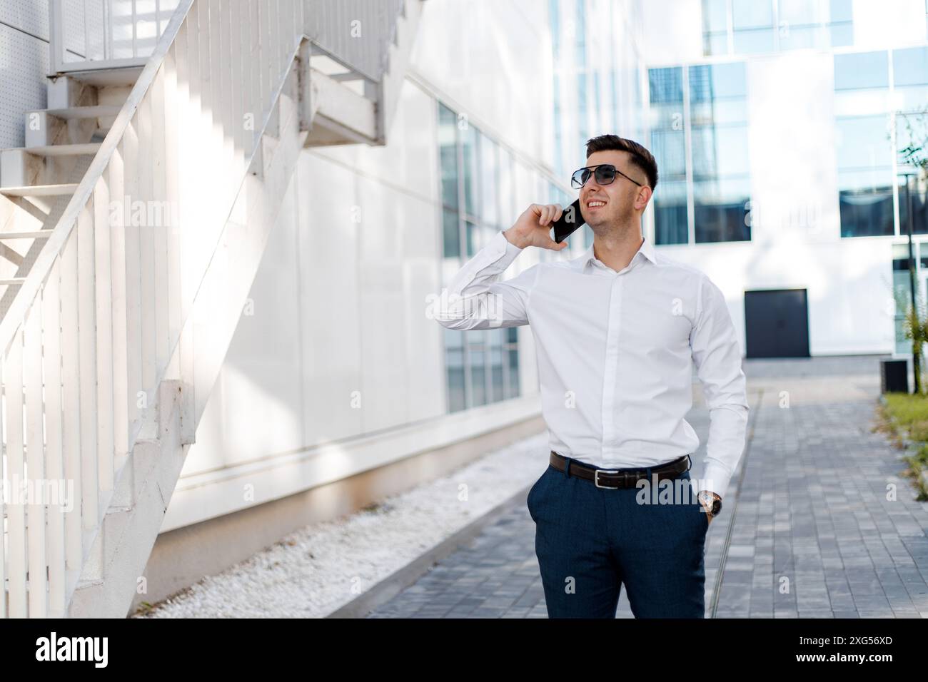 Ein Mann, der ein weißes Hemd trägt, führt ein Gespräch auf einem Handy und hält das Gerät mit einem fokussierten Ausdruck an sein Ohr. Stockfoto