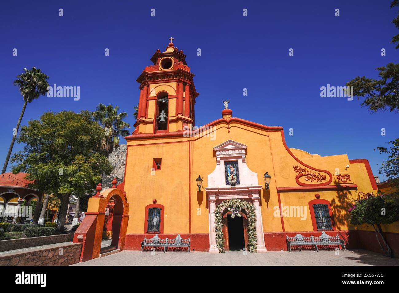 Die Kirche Parroquia San Sebastian mit dem massiven Felsberg Pena de Bernal dahinter im wunderschönen Kolonialdorf Bernal, Queretaro, Mexiko. Bernal ist eine malerische Kolonialstadt, bekannt für die Pena de Bernal, ein riesiger Monolith, der das winzige Dorf dominiert, das dritthöchste der Welt ist. Stockfoto