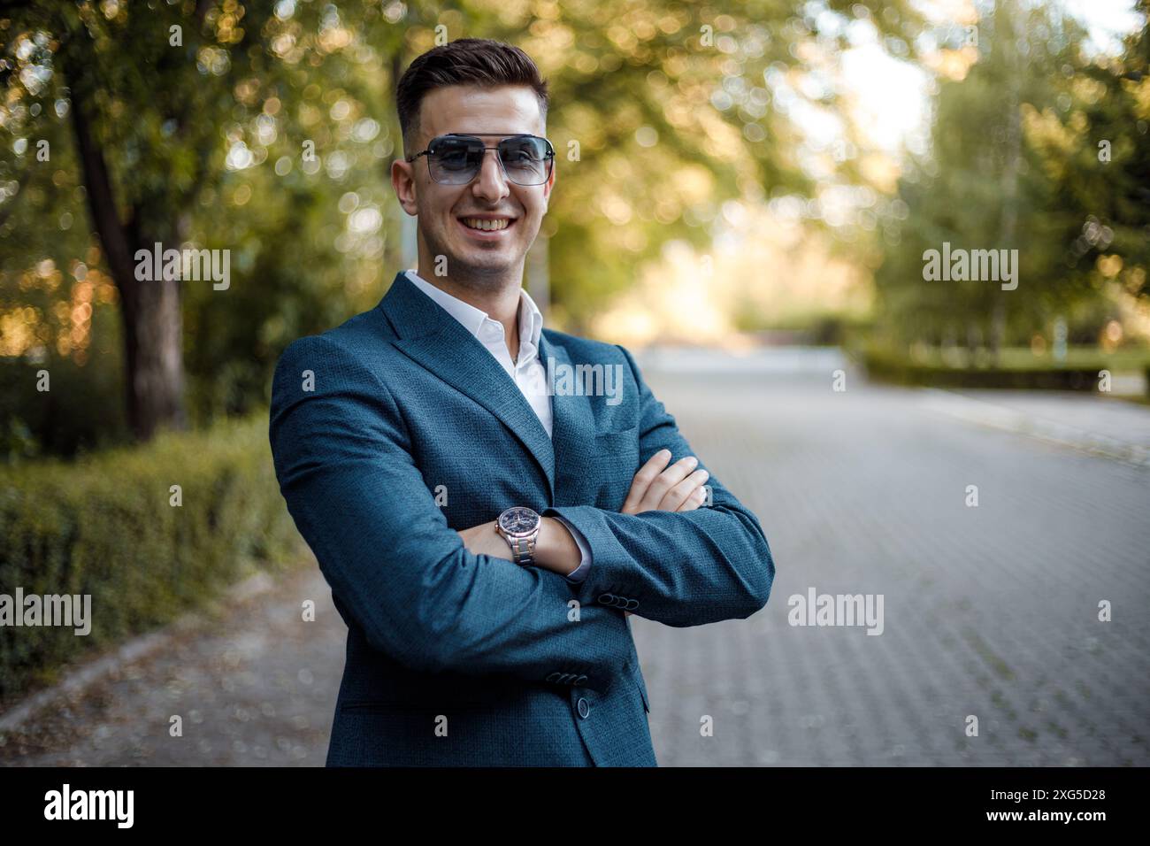 Ein Mann in Anzug und Sonnenbrille steht auf einer belebten Straße und blickt selbstbewusst nach vorne. Er scheint zu warten oder etwas zu beobachten. Stockfoto