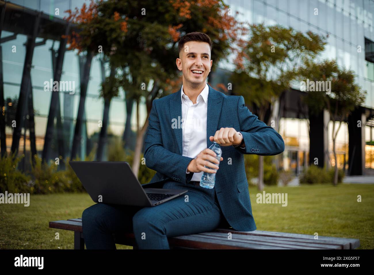 Ein Mann saß draußen auf einer Holzbank und arbeitete an einem Laptop. Er konzentriert sich auf seinen Bildschirm, möglicherweise tippt oder surft. Stockfoto