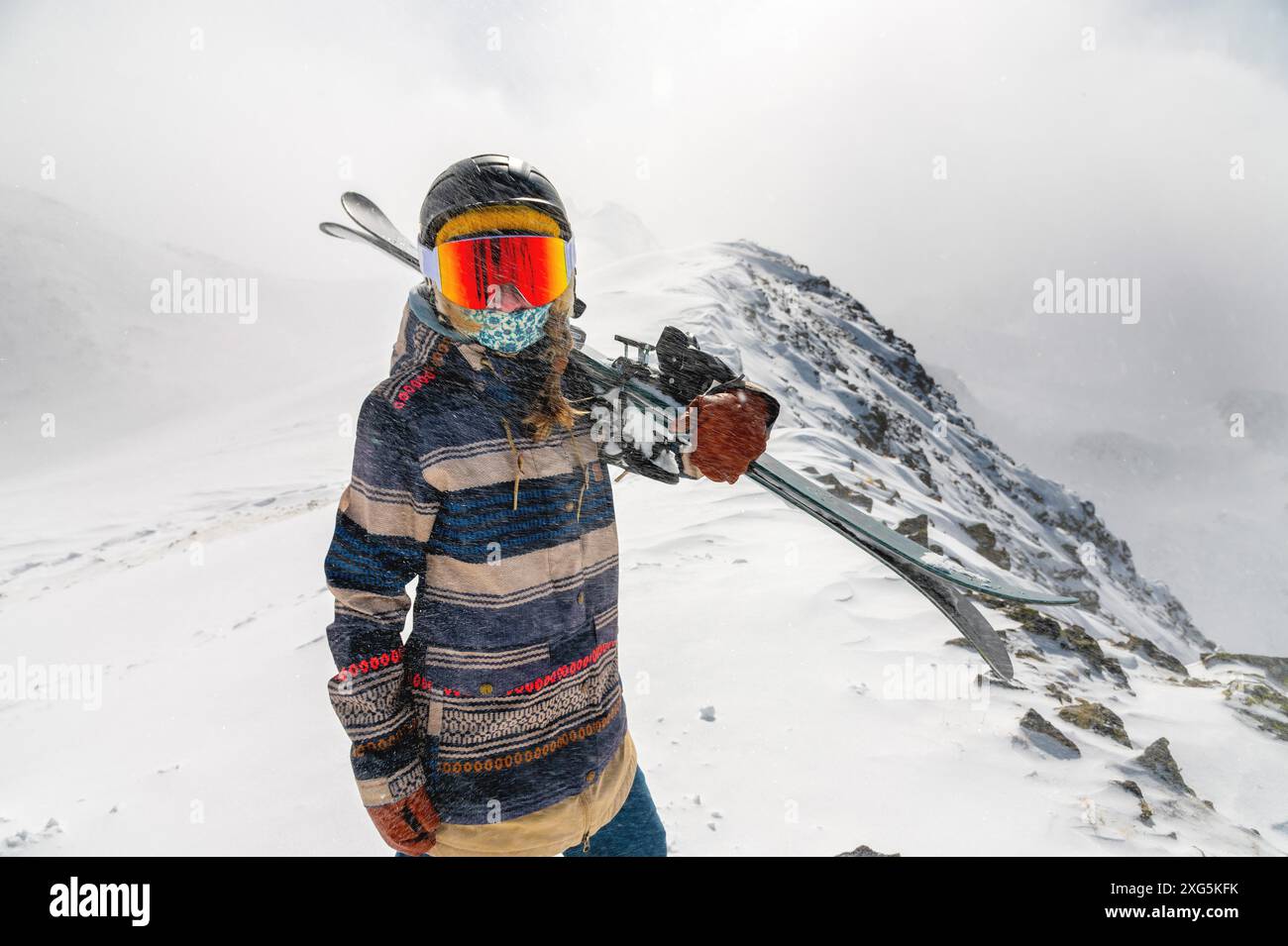 Porträt einer hübschen und aktiven Skifahrerin, die eine Maske trägt und Ski in der Hand hält, aktive Winterferien. Extreme Lifestyle-Konzept Stockfoto